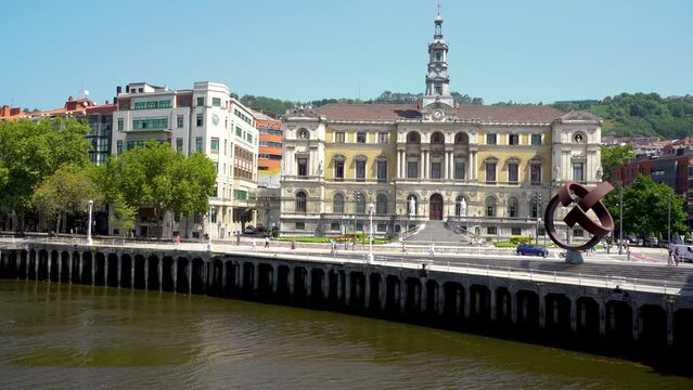 Bilbao, SPAIN - July 19 2022: Beautiful City Hall building of the of Bilbao city. In front of the building is the river Nervion. People walking on the promenade area. Stabilized static video.