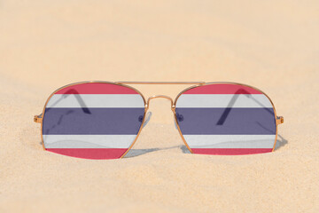 Sunglasses with glasses in the form of the flag of Thailand lie on the sand. The concept of summer holidays, travel and tourism in Thailand