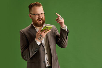 Bearded men, employees in glasses and suit talking on mobile phone against green studio background. Discussion. Concept of business, emotions, lifestyle, office, fashion, ad