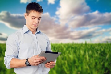 Happy farmer holds digital tablet against field.