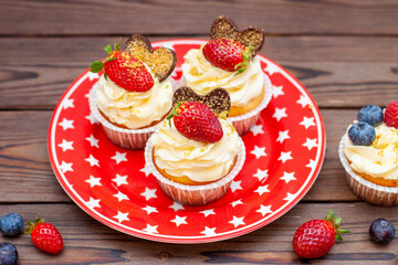 Set of vanilla cupcakes decorated with fresh strawberries, blueberries, chocolate hearts and golden sprinkles on red star plate
