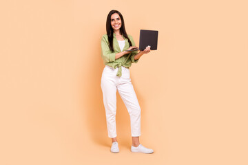 Full length photo of lovely positive satisfied woman wear green shirt holding laptop write email isolated on beige color background