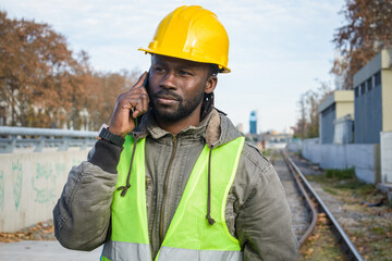 adult man of african ethnicity builder engineer talking on the phone on the railway tracks.