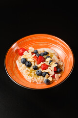 Oatmeal with blueberries, almonds and strawberries in an orange plate.