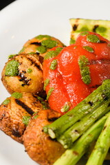 Assorted grilled vegetables with pesto sauce on a white plate.
