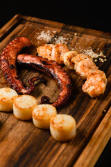 Assorted grilled seafood on wooden cutting board, dark background.