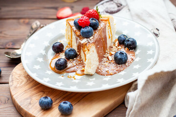Slice of vanilla cheesecake with salted caramel sauce, fresh raspberry, blueberry and nuts on grey star plate, close up view