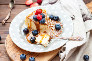 Slice of vanilla cheesecake with salted caramel sauce, fresh raspberry, blueberry and nuts on grey star plate, close up view