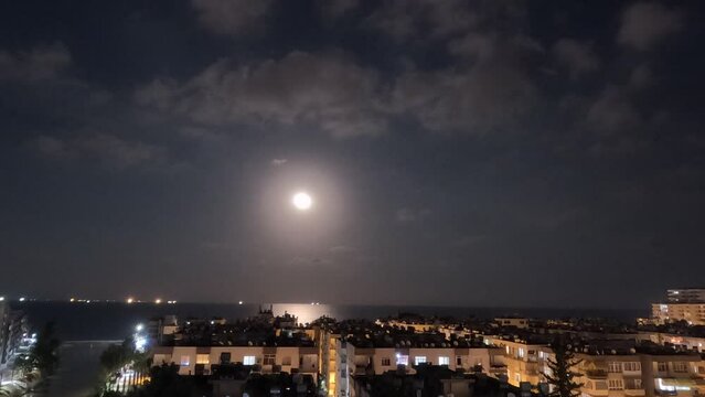 full moonrise over the sea in the clouds over the seaside city. timelapse