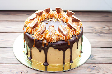 Peanut butter cream cake with melted chocolate, candy bars, bites of peanuts and salted caramel on...