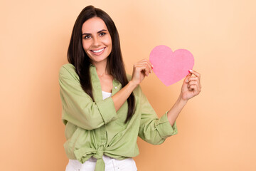 Photo of optimistic stunning girl with straight hairstyle dressed green blouse fingers hold large heart isolated on beige color background