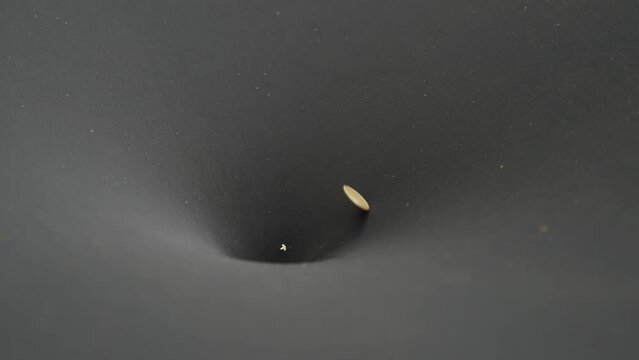 Coin spirals down black funnel and falls into hole in center. Close up of scientific physics experiment simulating black hole in space for visual demonstration for education students at school.