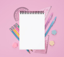 Flatlay composition with blank notepad and school stationery on a pink background. Back to school. Mockup. Top view. Copy space.