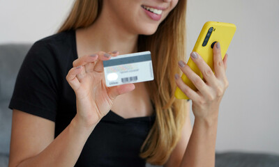 Satisfied young woman doing online transaction with her smartphone and credit card comfortably from...