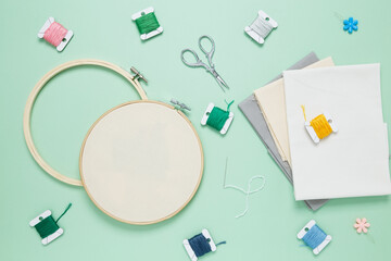 Embroidery set fot stitching. Beige cotton cloth in embroidery hoop on green background with fabric, colorful threads, scissors and needls. Indoor hobby concept with copy space, top view © matucha12