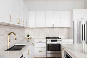 A kitchen detail with white cabinets, gold hardware and faucet, marble countertops, and a brown...