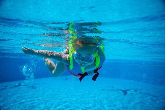 Portrait of little girl swimming underwater in goggles and vest in pool. Summer vacation
