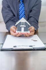 Fototapeta na wymiar Real estate agents hand holding home model, explains the business contract for signing a business contract, renting, buying, mortgage, loan or home insurance