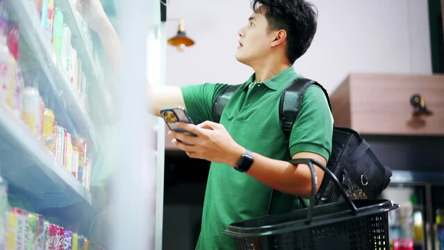 Grocery delivery service shopper with insulated delivery bag buying items for customers at supermarket. Asian man rider selecting food supply for client order. Personal shopper concept