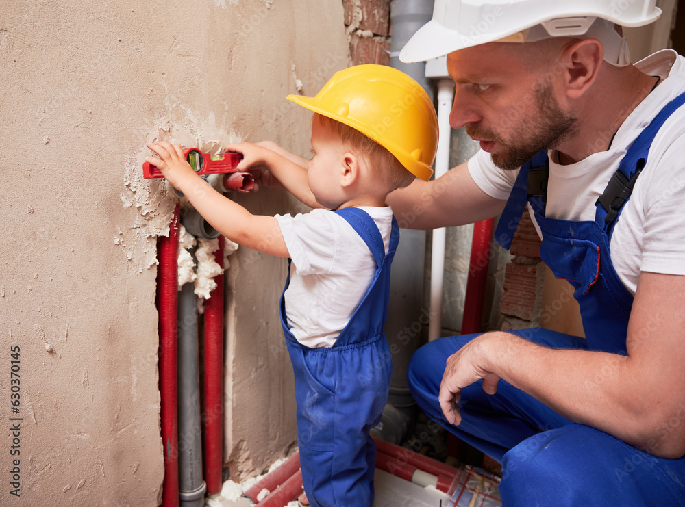 Wall mural male plumber and child measuring pipes level with building instrument. man and little boy in safety 