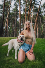 Beautiful girl with a dog on the lawn. White labrador on a walk with a woman in the park. vertical frame 