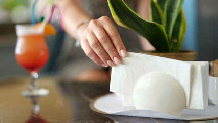 Woman takes paper napkin from ceramic napkin holder on served table. Napkin holder in cafe