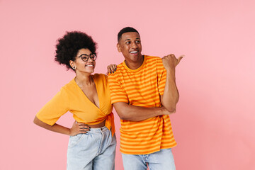 African man and woman looking away and pointing finger at copy space isolated over pink background