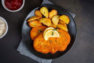 Chicken schnitzel with sauce, fried potatoes and lemon in a plate