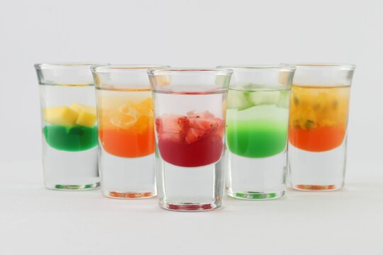 Glasses filled with vodka, each topped with passion fruit, strawberry, apple, and mango