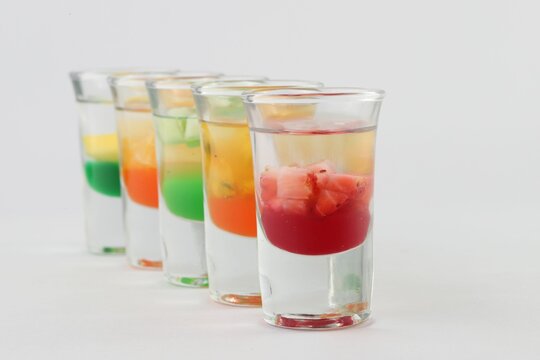 Glasses filled with vodka, each topped with passion fruit, strawberry, apple, and mango