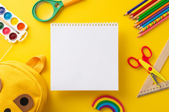 Attract attention from parents and educators alike with top-down image of blank notepad page overflowing with array of colorful school supplies. Perfect for educational campaigns on yellow backdrop