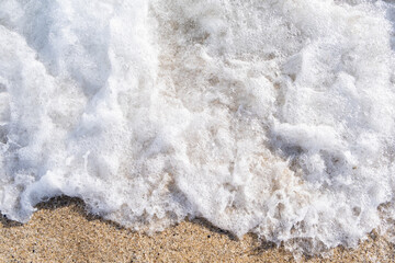 A soft wave runs on a sandy shore on a summer day. Empty space can be used as background for display or montage your top view products.