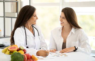 Happy mature caucasian doctor nutritionist in white coat advises young woman at table with organic...