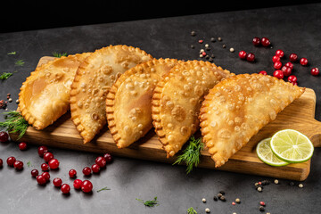 Uzbek Tatar cuisine. Fried chebureks, pies from air dough and meat on a wooden board, on a dark background.