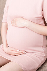 Pregnant Lady Having Massaging Lower belly Sitting On Sofa Indoor. Pregnancy Problems Concept. Maternity healthcare