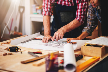 Small business furniture owner and professional architect interior designer working in carpenter workshop with blueprint and tablet discussing about home furnishing design project.