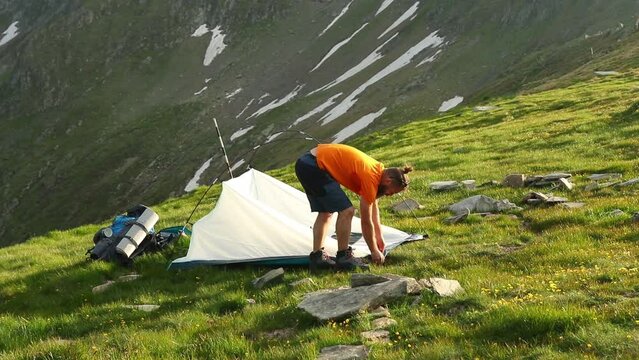 Caucasian man setting up a tent in the green mountains with a landscape in the background