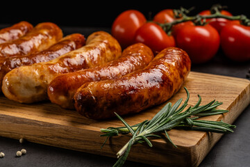 German cuisine. Juicy fried chicken, beef and pork sausages lie on a wooden board, on a black background.