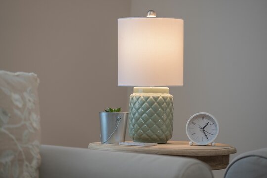 Close up image of a wooden table featuring a clock with a white face and a modern lamp