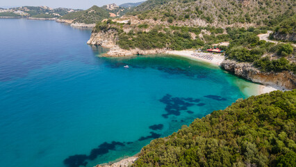 Fototapeta na wymiar Aerial view of sea bay, sandy beach with umbrellas, trees, mountain at sunny day in summer. Blue lagoon in Syvota Greece. Tropical landscape with island, white sandy bank, blue water. Top view
