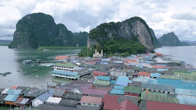 Aerial of a small village in Tha Yu, Thailand with mountains and a cloudy sky in the background