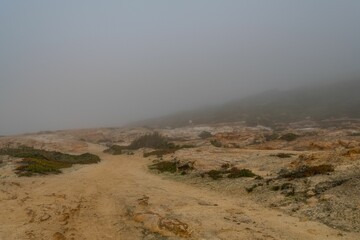 Barren desert landscape situated on the edge of a steep cliff, shrouded in a dense layer of fog