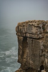 Vertical shot of a rocky cliff by the sea covered in fog