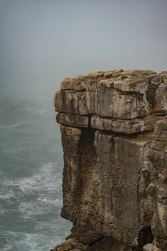 Vertical shot of a rocky cliff by the sea covered in fog