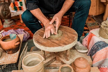 Male potter working on a clay object using his hands on a wooden wheel