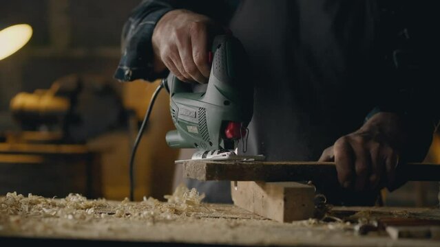 Wood shavings, Workshop worker Carefully cuts a hole with an electric jigsaw with a wood saw In the workshop Follow-up shot Junior specialist Works at a carpentry table In a carpentry shop, workpiece