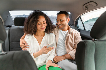 Smiling Middle Eastern Couple in Taxi Embracing And Using Smartphone