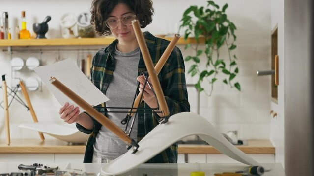 Young woman on her own Concentrated Studying furniture assembly instruction while assembling a chair Home interior, Camera in motion Active young female worker Assembling furniture, household chores