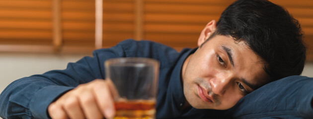 Alcoholism, depressed asian young man sleep on table while drinking alcoholic beverage, holding glass of whiskey alone at night. Treatment of alcohol addiction, suffer abuse problem alcoholism concept