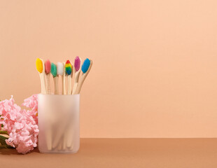 Eco friendly bamboo toothbrushes with colorful bristles in a cup on a beige background. Copy space...
